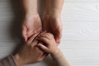 Photo of Family holding hands together at white wooden table, top view. Space for text
