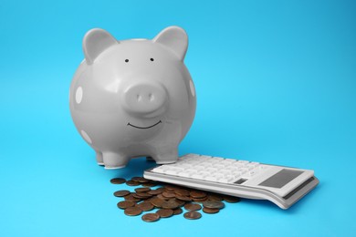 Photo of Piggy bank, coins and calculator on light blue background