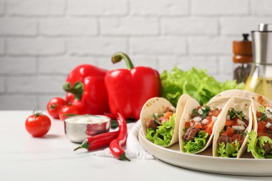 Photo of Delicious tacos with meat and vegetables on white table against light brick wall, closeup