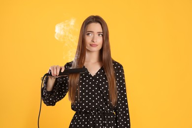 Image of Upset young woman with flattening iron on yellow background. Hair damage