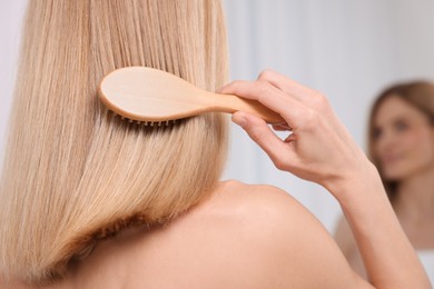 Woman brushing her hair near mirror in room, closeup