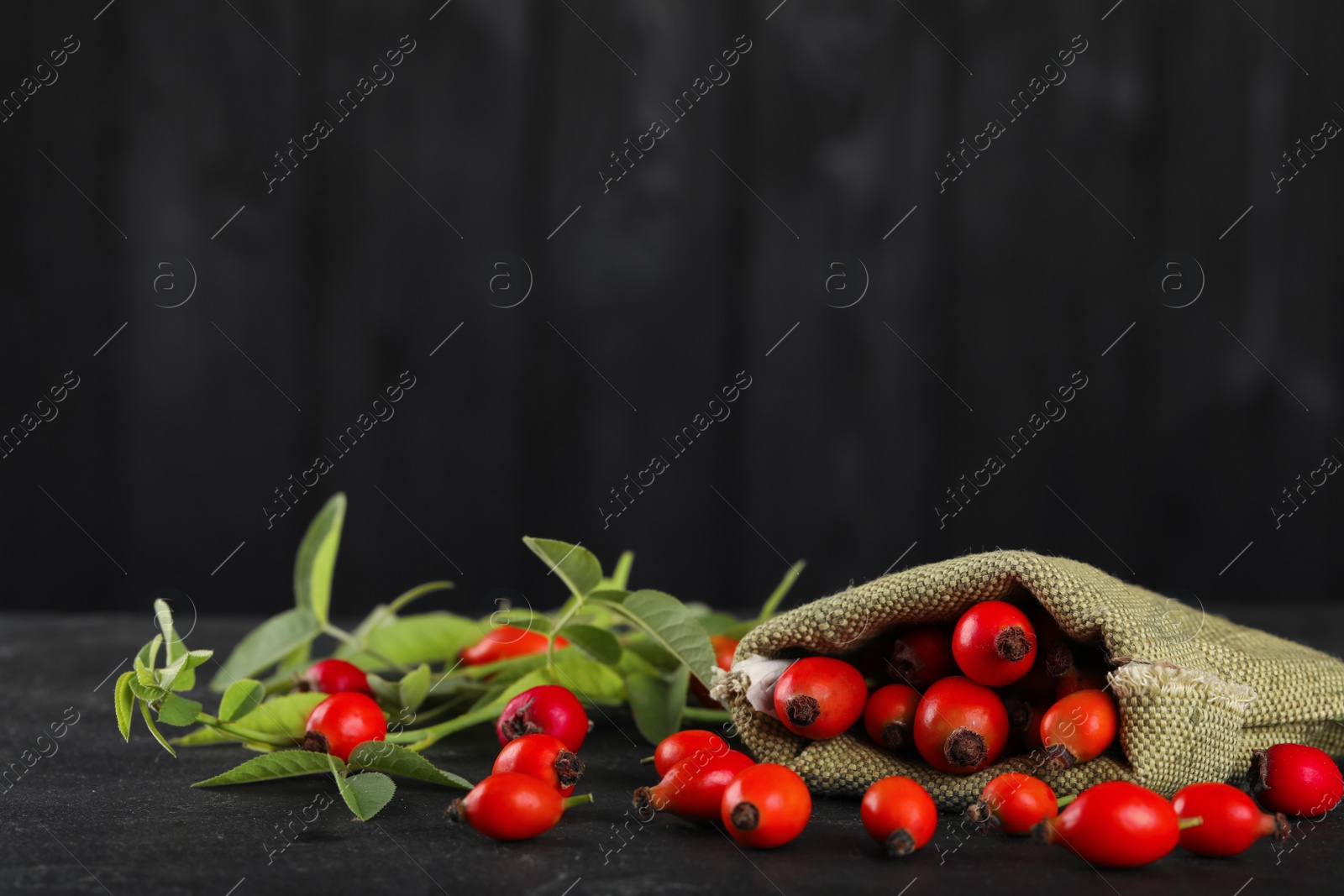 Photo of Ripe rose hip berries with green leaves on black table. Space for text