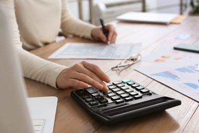 Photo of Tax accountant with calculator working at wooden table, closeup