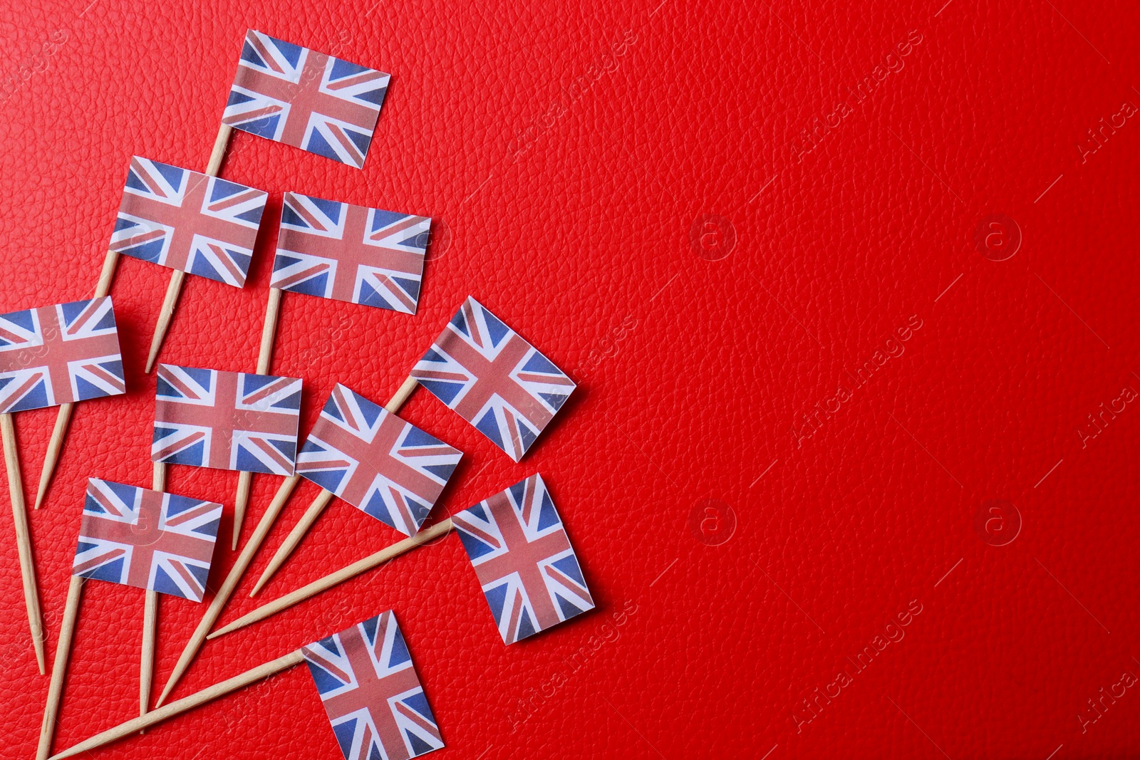 Photo of Small paper flags of United Kingdom on red textured background, flat lay. Space for text