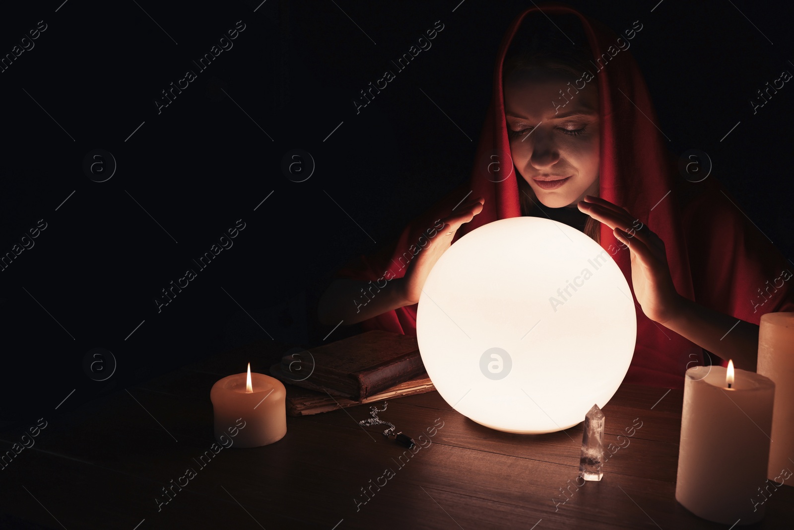 Photo of Soothsayer using glowing crystal ball to predict future at table in darkness, space for text. Fortune telling