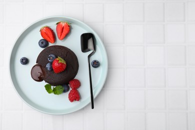 Photo of Plate with delicious chocolate fondant, berries and mint on white tiled table, top view. Space for text