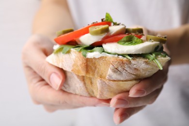 Woman holding tasty bruschetta with tomatoes, mozzarella and olives on white background, closeup