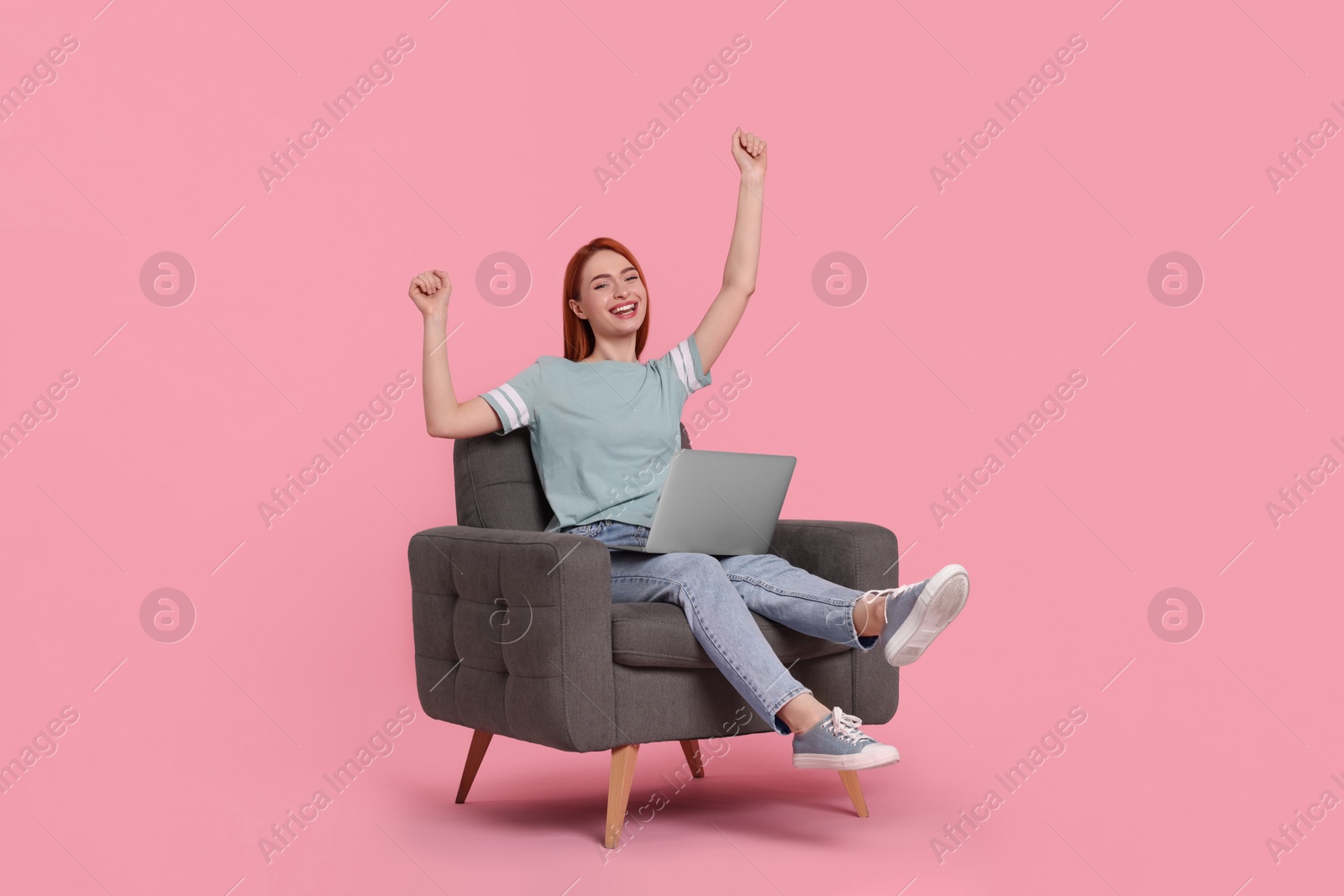 Photo of Happy young woman with laptop sitting in armchair on pink background