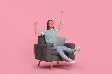 Photo of Happy young woman with laptop sitting in armchair on pink background