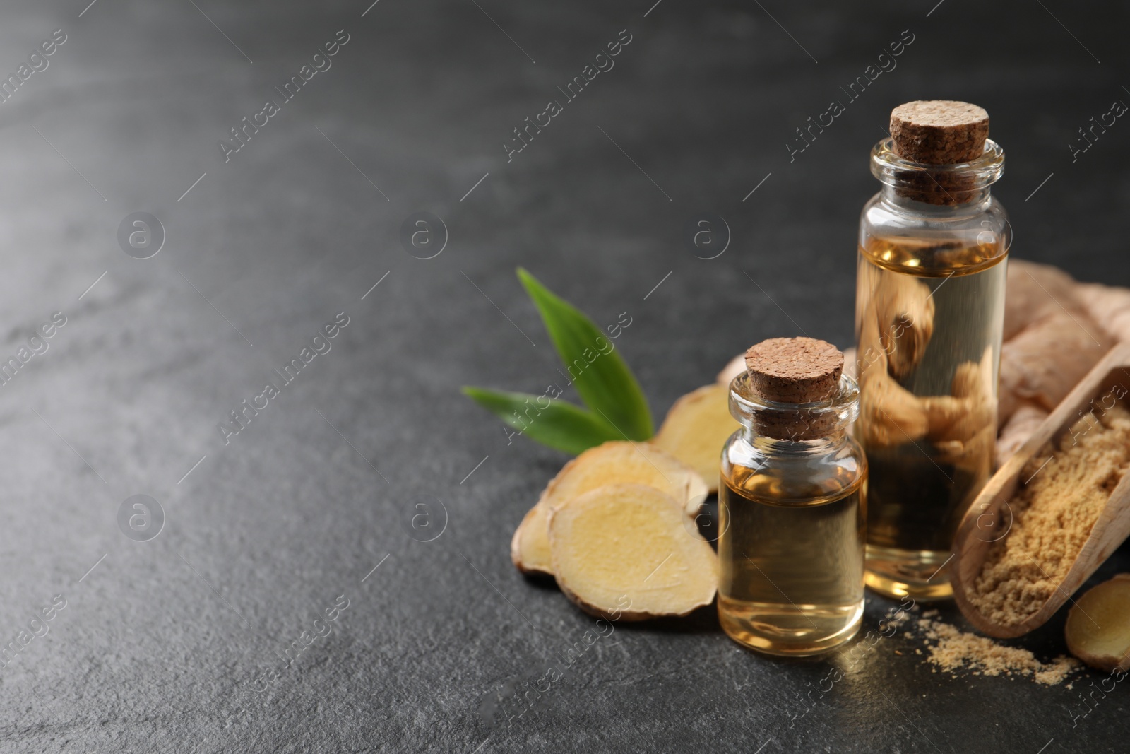 Photo of Glass bottles of essential oil, ginger powder and root on dark table, space for text