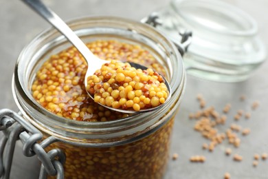 Photo of Whole grain mustard in jar and spoon on wooden table, closeup. Space for text