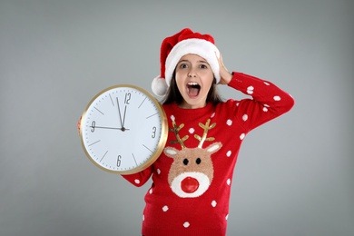 Girl in Santa hat with clock on grey background. New Year countdown