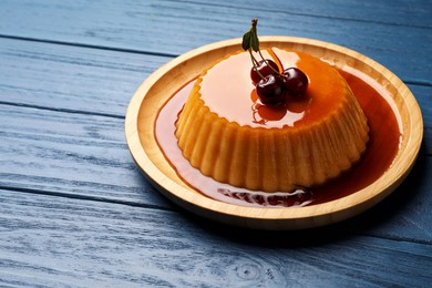 Photo of Delicious pudding with caramel and cherries on blue wooden table