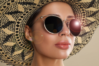 Beautiful young woman wearing sunglasses and hat on beige background, closeup