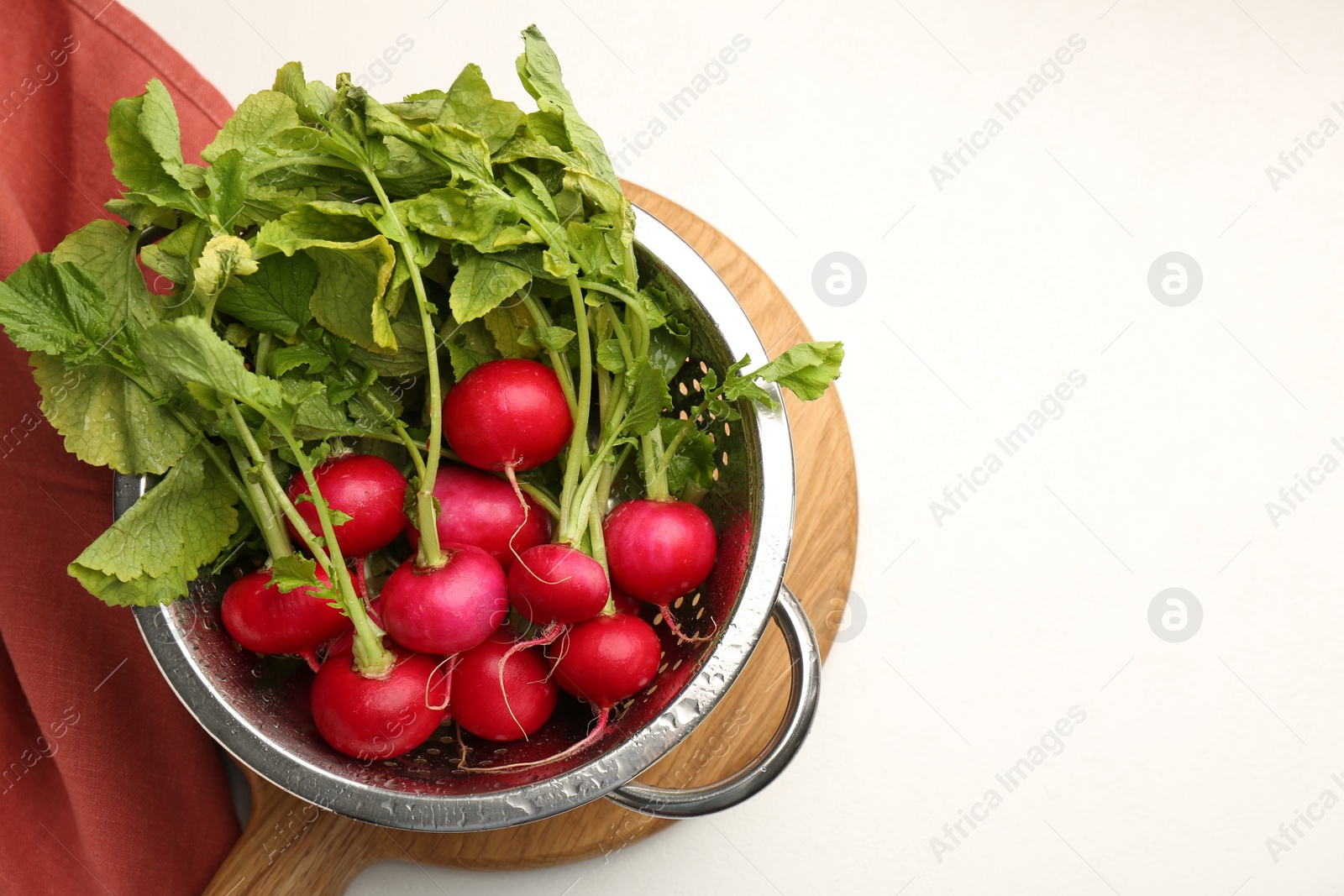 Photo of Wet radish in colander on white table, top view. Space for text