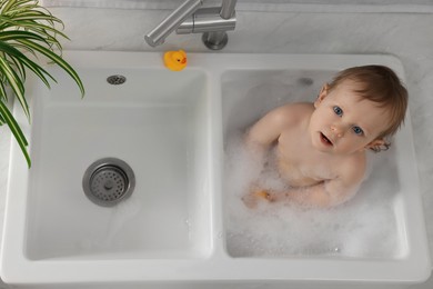 Cute little baby bathing in sink indoors, top view