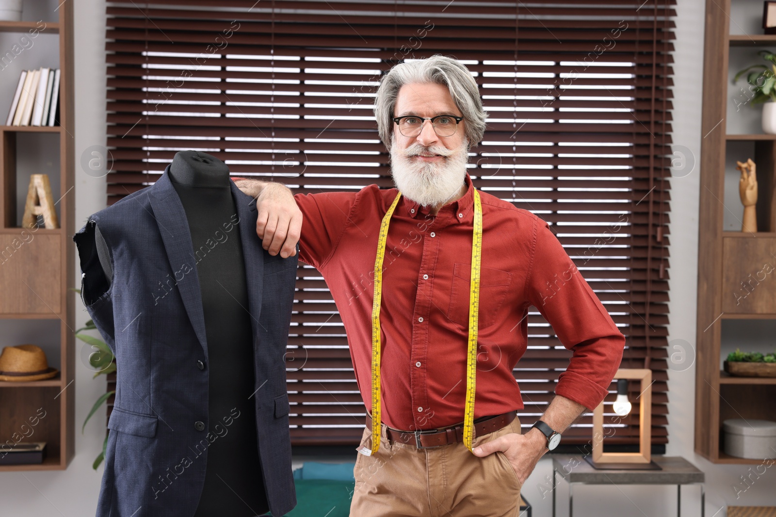 Photo of Professional tailor with measuring tape near mannequin in workshop