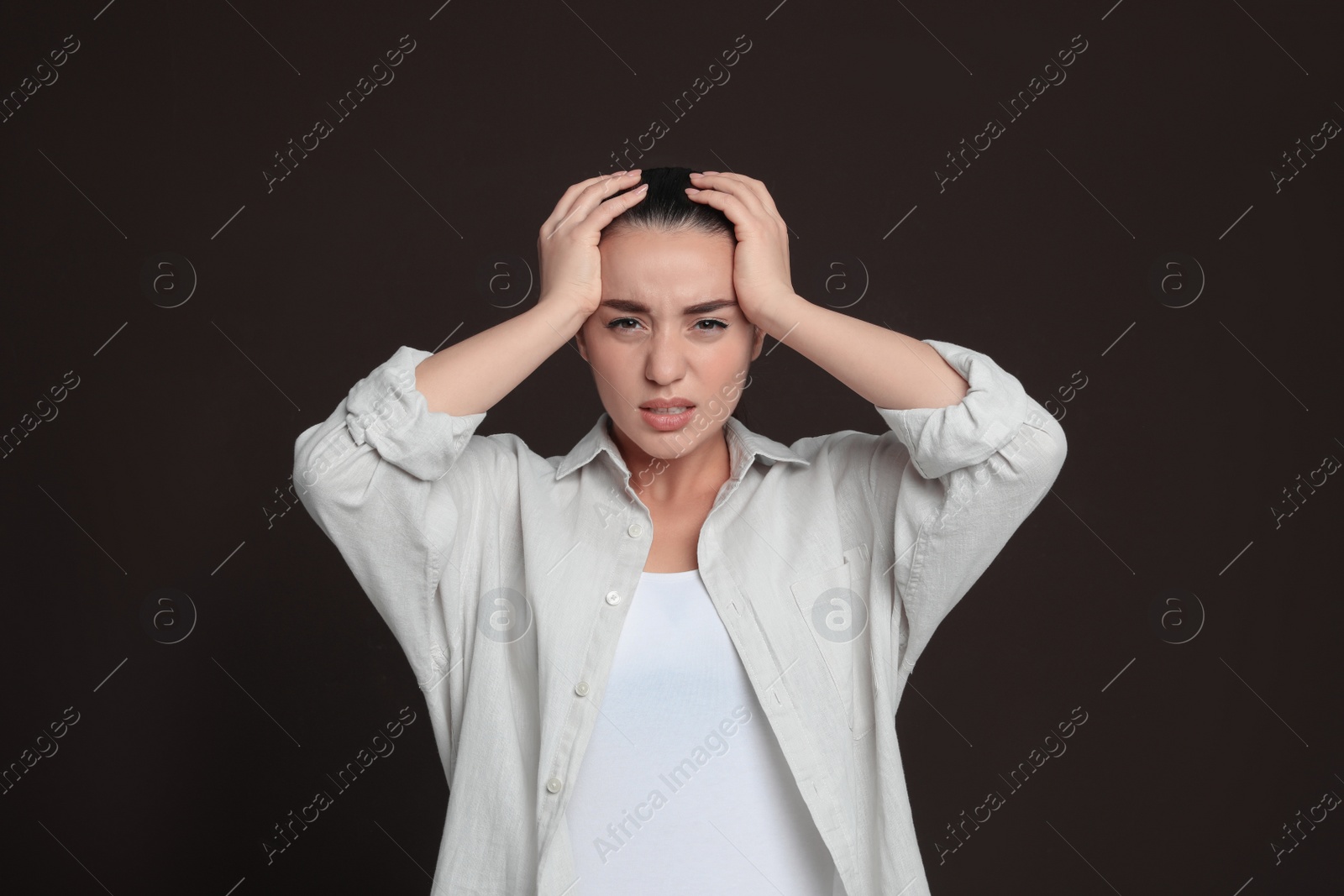 Photo of Young woman suffering from headache on dark brown background