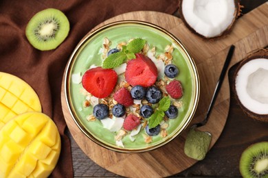 Photo of Tasty matcha smoothie bowl served with fresh fruits and oatmeal on wooden table, flat lay. Healthy breakfast