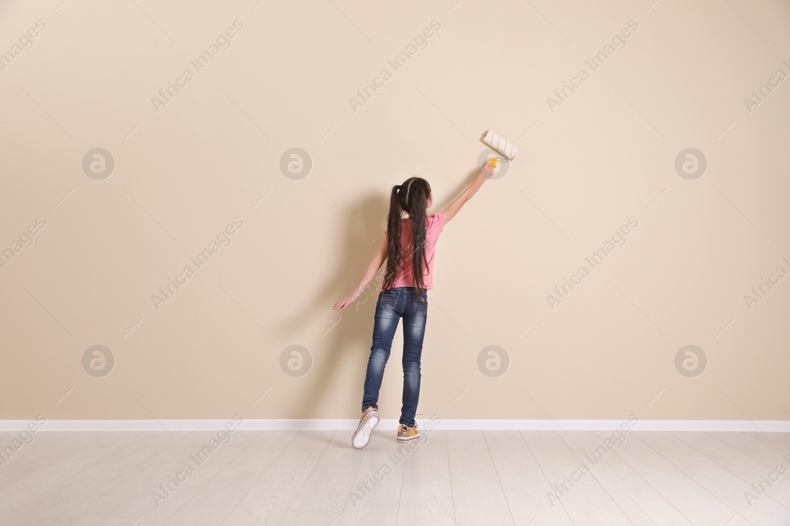 Photo of Child painting color wall with roller brush