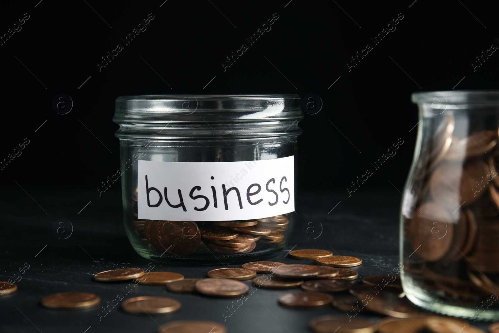 Photo of Glass jar with coins and tag BUSINESS on black table