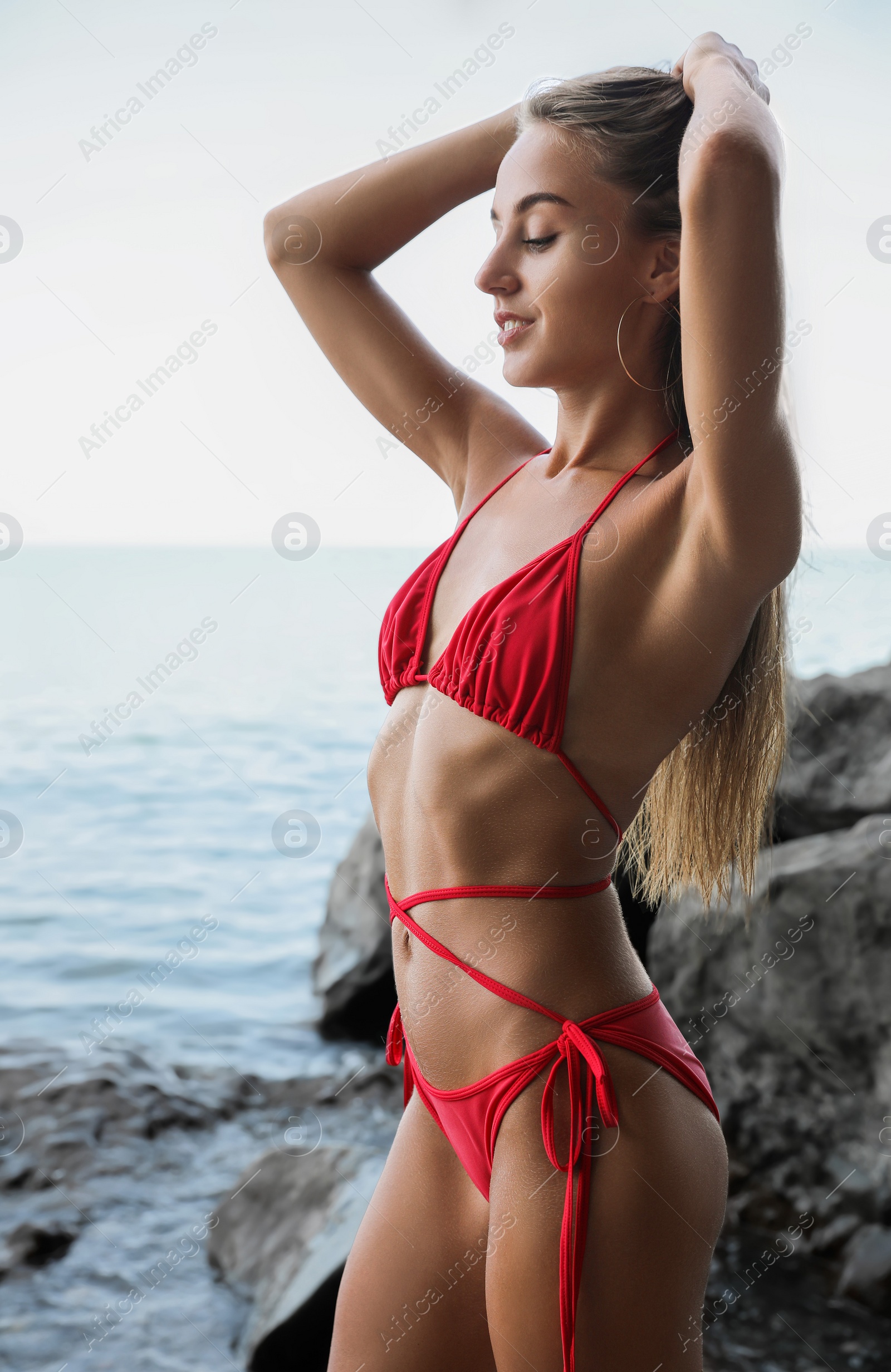 Photo of Beautiful young woman in stylish bikini on seashore, space for text