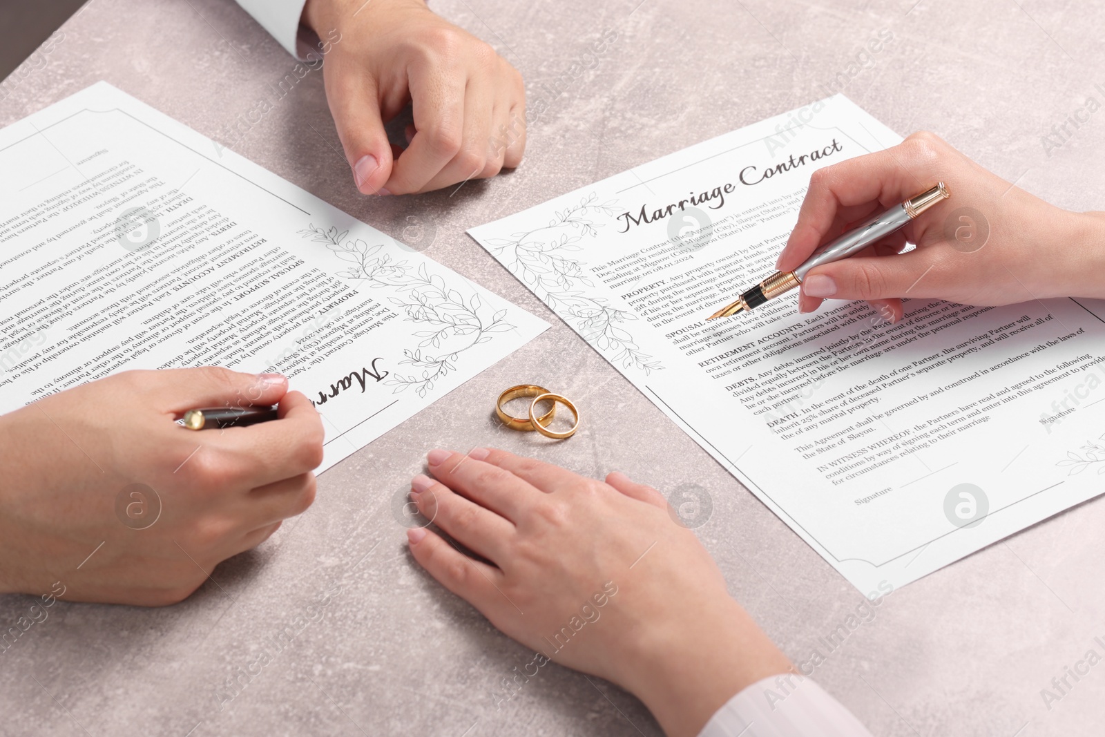 Photo of Man and woman signing marriage contract at light grey table, closeup