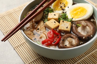 Photo of Bowl of delicious ramen and chopsticks on grey table, closeup. Noodle soup