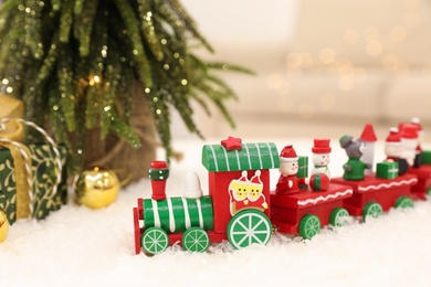 Photo of Bright toy train on artificial snow near small Christmas tree