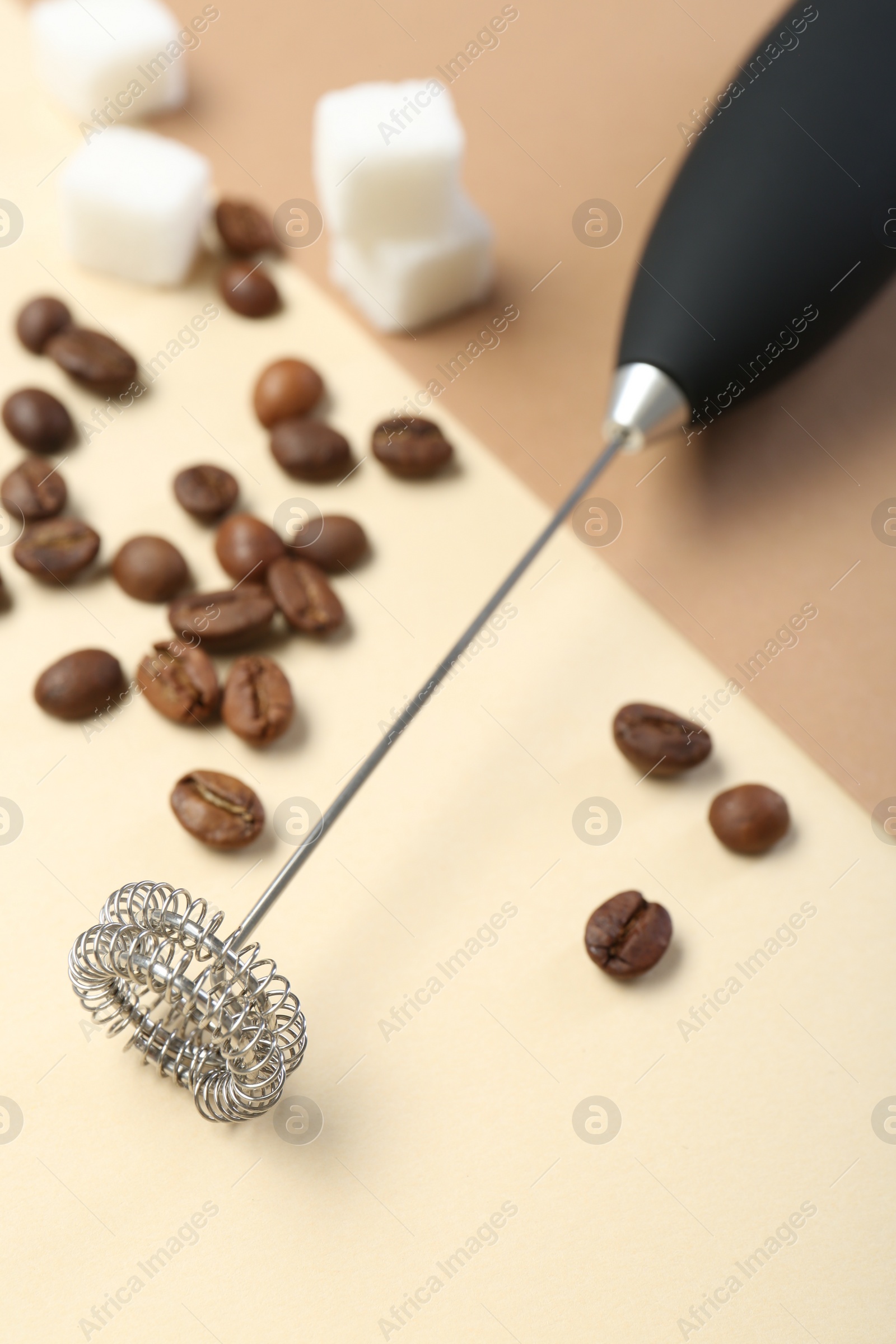 Photo of Milk frother wand, coffee beans and sugar cubes on color background, closeup