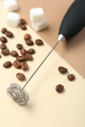 Milk frother wand, coffee beans and sugar cubes on color background, closeup