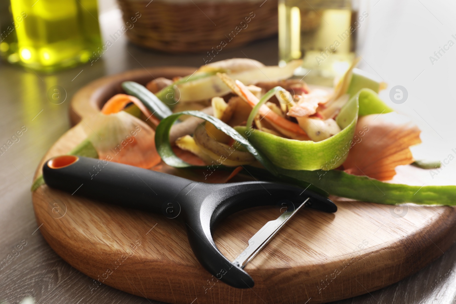 Photo of Peels of fresh vegetables and peeler on wooden table, closeup