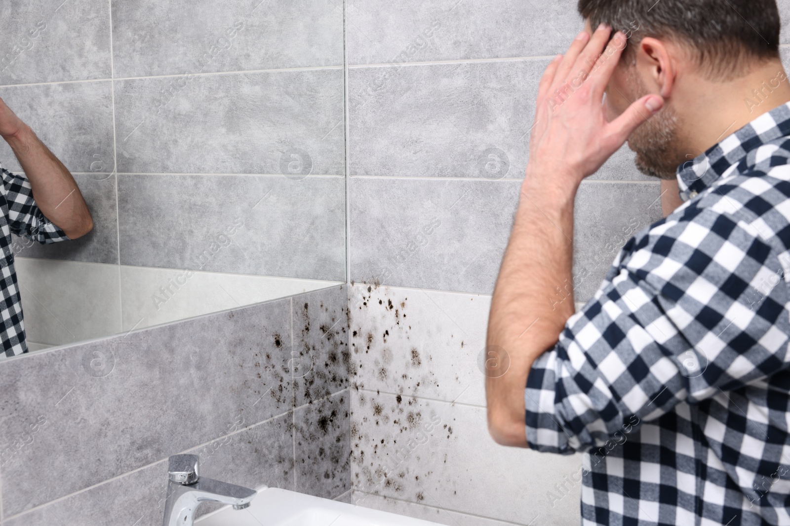 Image of Man looking at affected with mold walls in bathroom