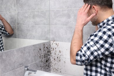 Man looking at affected with mold walls in bathroom