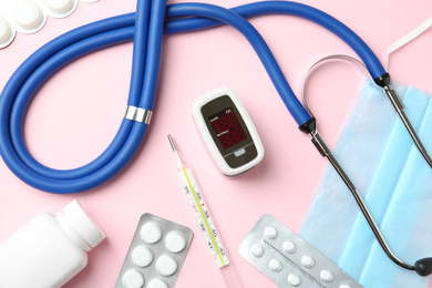 Flat lay composition with fingertip pulse oximeter and medical items on pink background