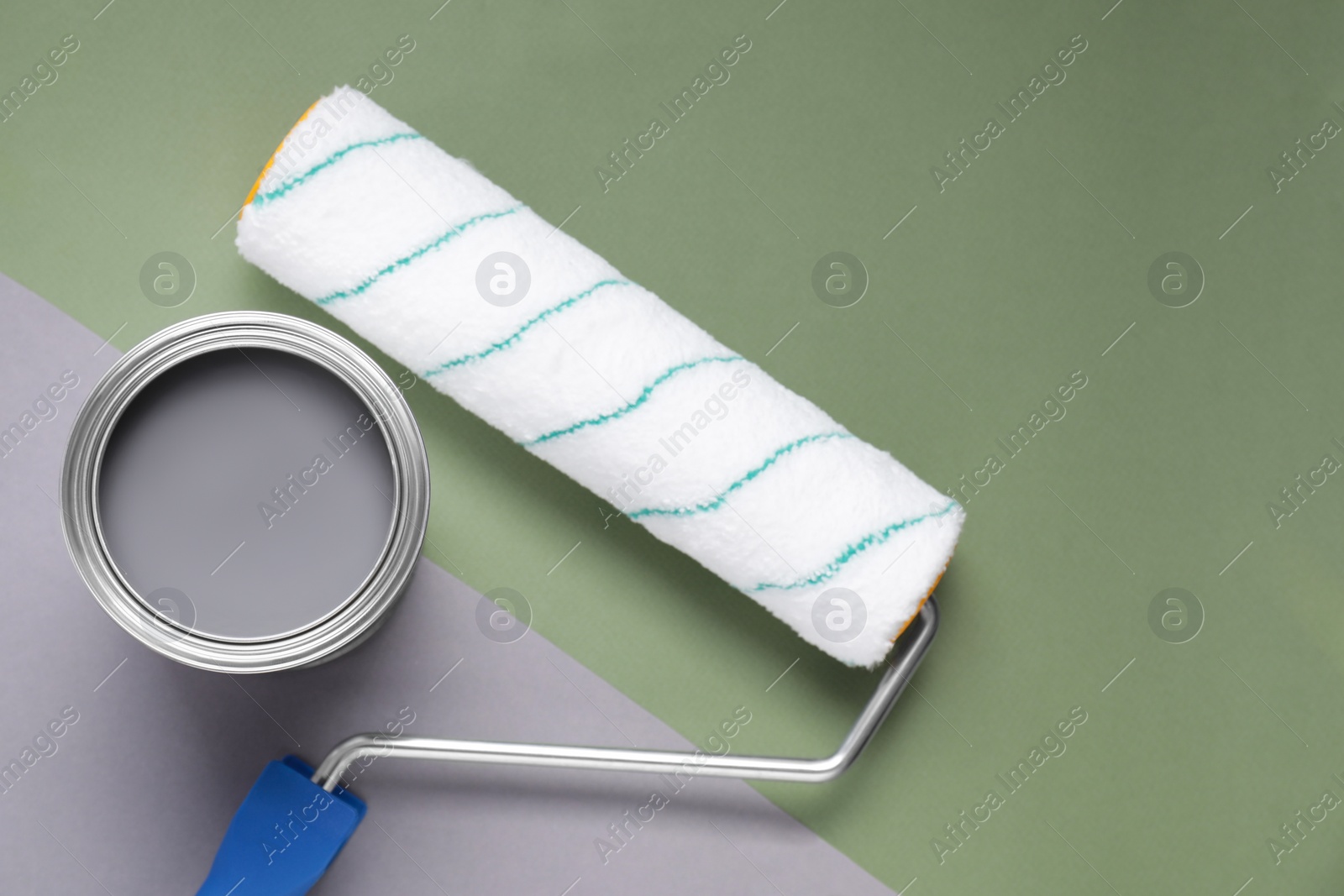 Photo of Can with gray paint and roller on light green background, flat lay