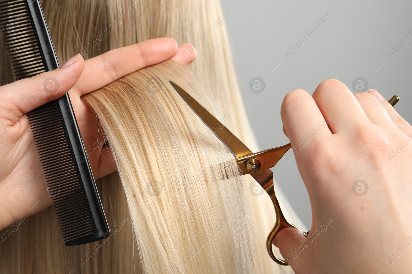 Photo of Hairdresser cutting client's hair with scissors on light grey background, closeup