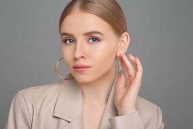 Beautiful young woman with elegant earrings on gray background