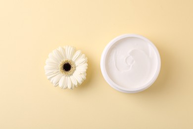 Photo of Moisturizing cream in open jar and gerbera flower on beige background, flat lay. Body care product