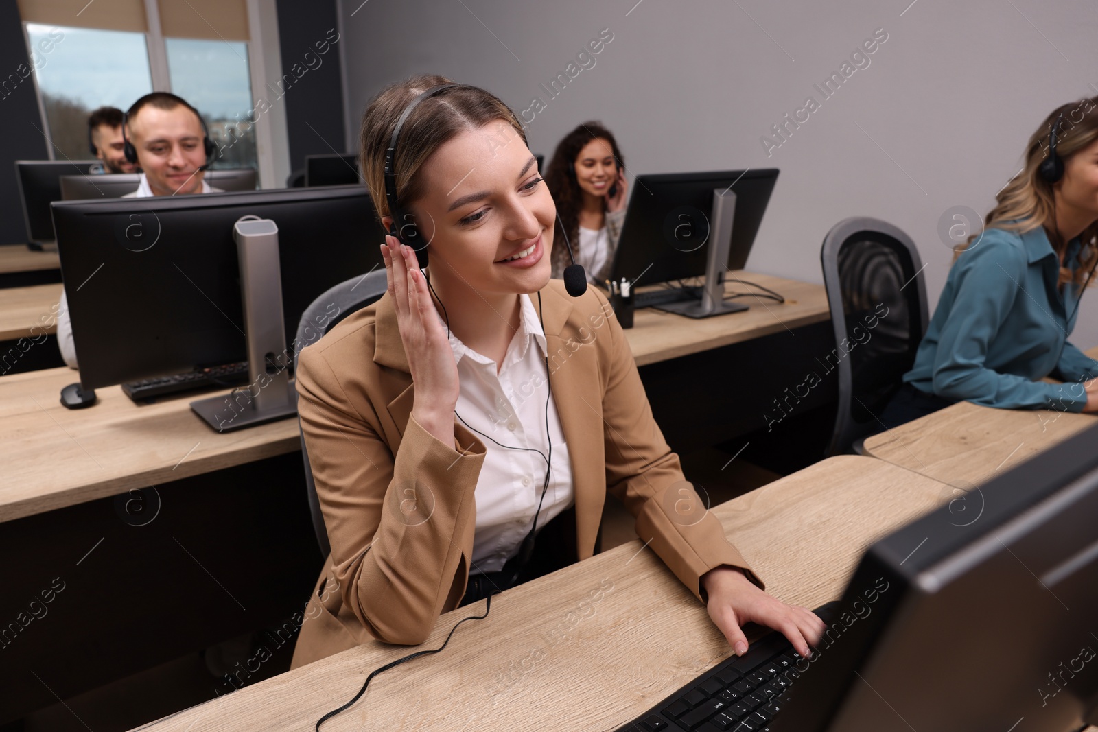 Photo of Call center operators working in modern office, focus on young woman with headset