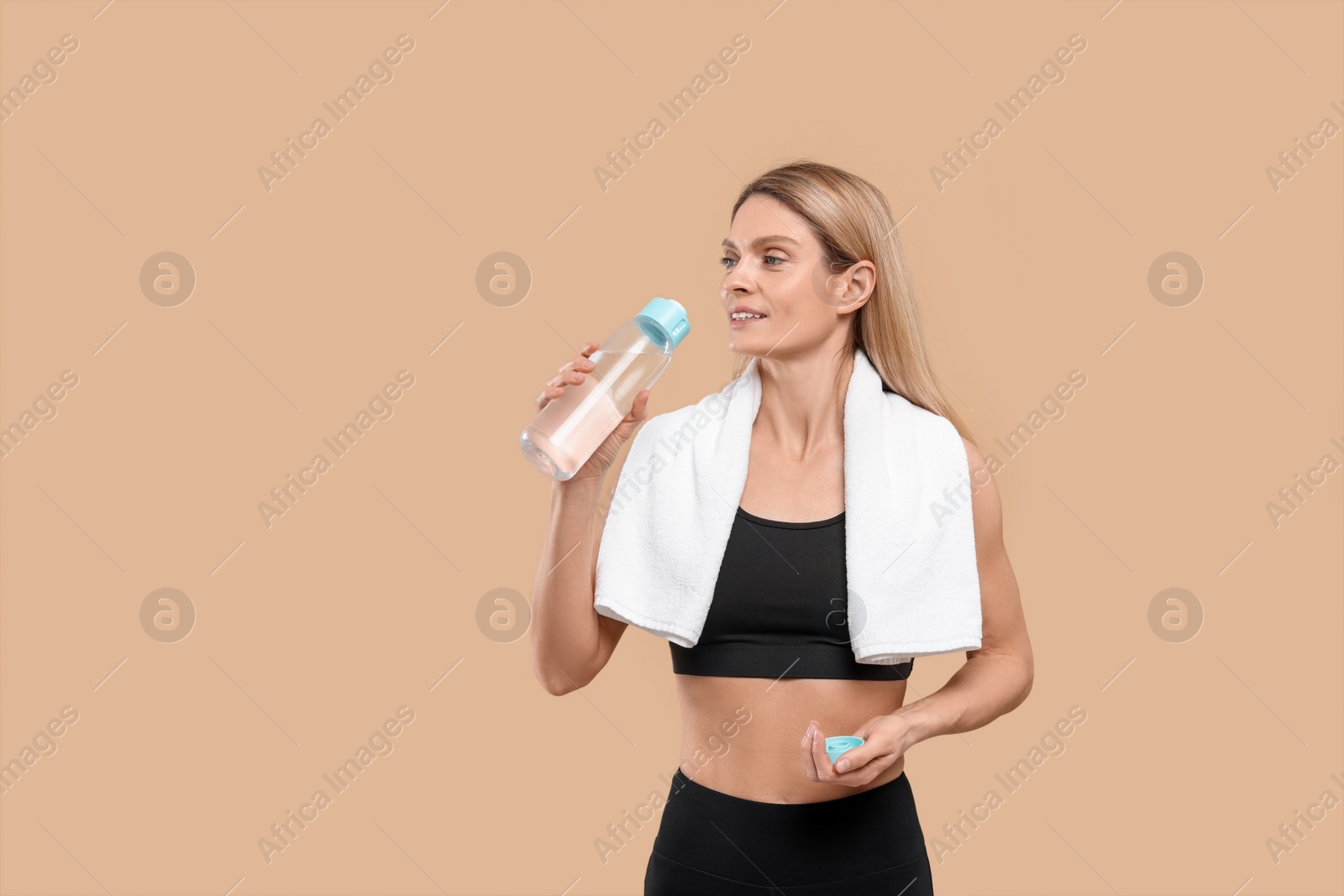 Photo of Athletic woman with bottle of water and white towel on beige background, space for text