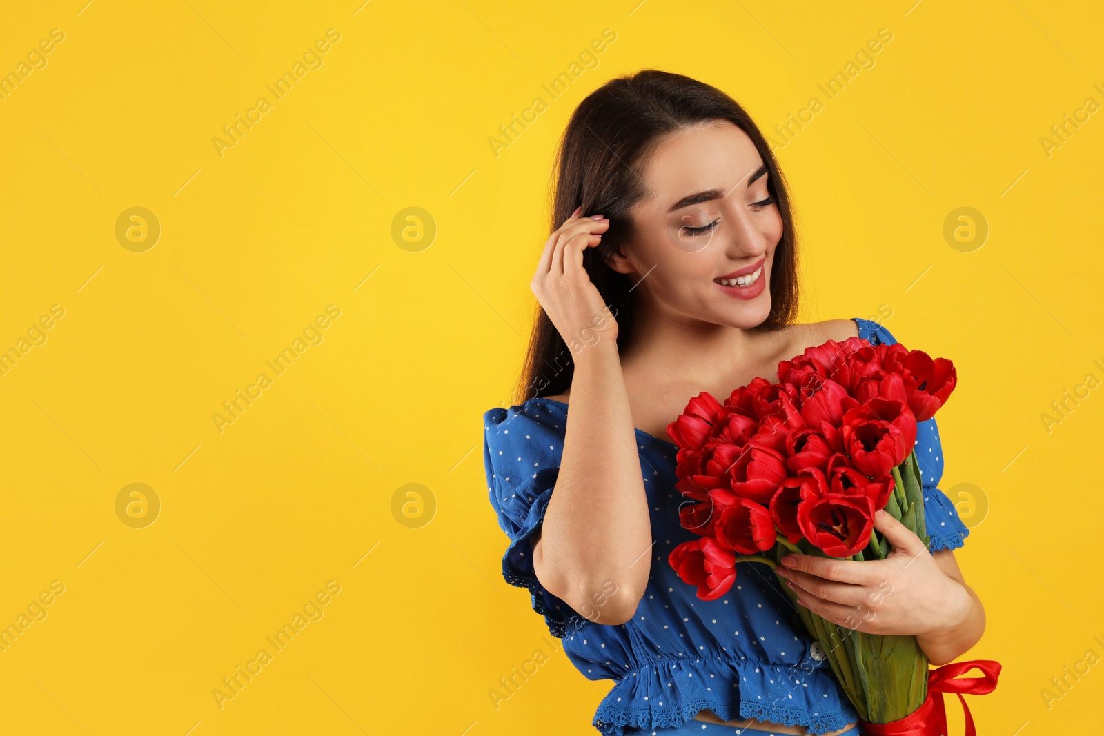 Photo of Happy woman with red tulip bouquet on yellow background, space for text. 8th of March celebration