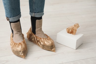 Photo of Woman wearing shoe covers onto her boots indoors, closeup