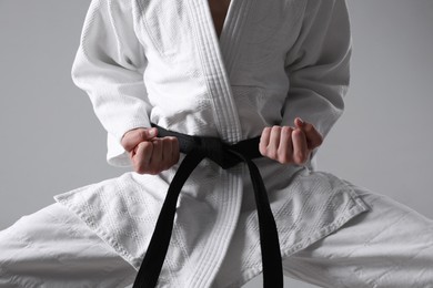 Martial arts master in keikogi with black belt on grey background, closeup