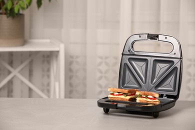 Photo of Modern grill maker with sandwiches on light grey table indoors, space for text