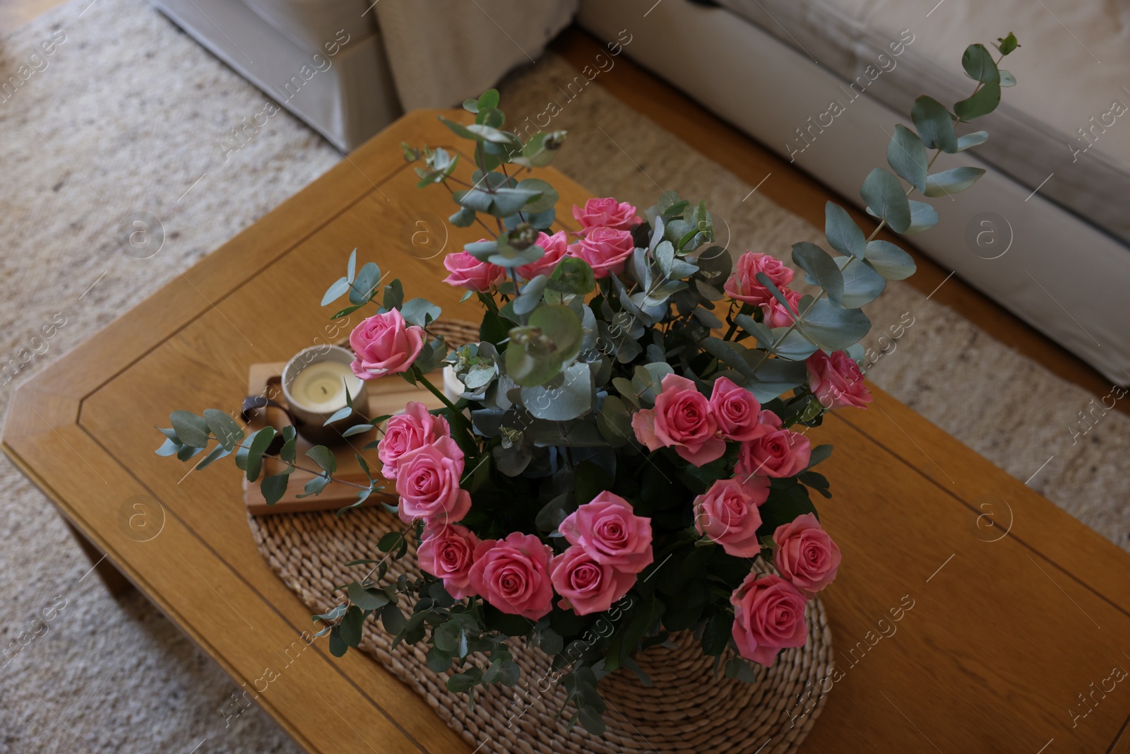 Photo of Beautiful bouquet of roses and eucalyptus branches in vase near candle on wooden table indoors, above view