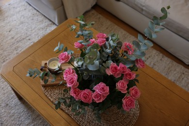 Beautiful bouquet of roses and eucalyptus branches in vase near candle on wooden table indoors, above view