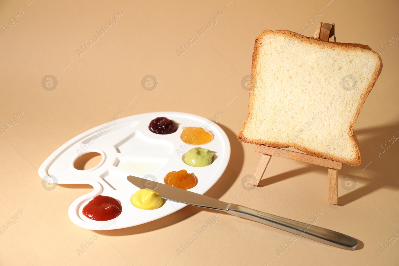 Photo of Slice of bread on small easel and palette with different sauces against beige background