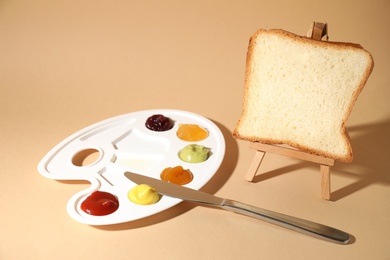 Photo of Slice of bread on small easel and palette with different sauces against beige background