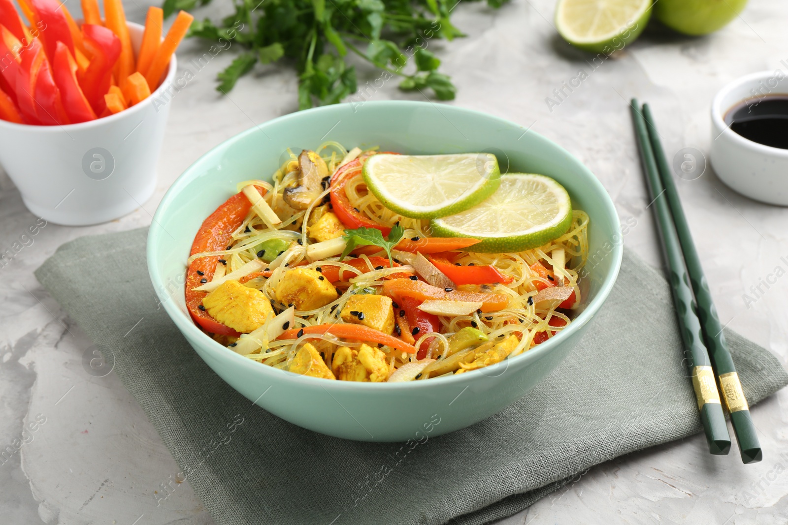 Photo of Stir-fry. Delicious cooked noodles with chicken and vegetables in bowl served on gray textured table